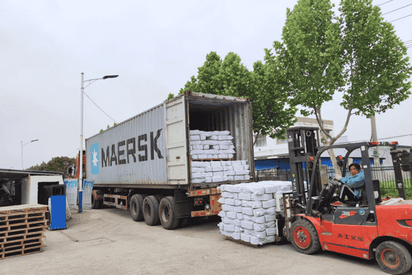 Forklift loading white fabric bales into a truck outdoors.