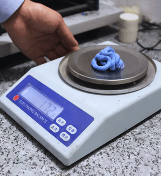 Lab technician weighing a sample of blue fiber on a digital scale for textile analysis.