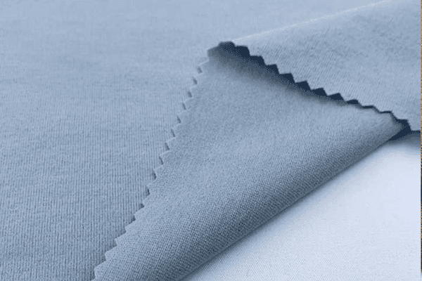 Close-up view of a light blue knitted fabric with a zigzag-cut edge, showcasing its smooth texture and flexibility.