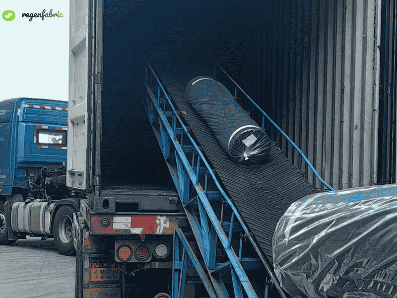 Fabric rolls being loaded into a shipping container via conveyor.