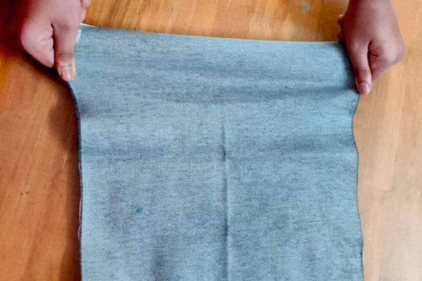 A pair of hands stretching a folded piece of light blue fabric on a wooden surface.